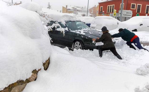 Un hombre y una mujer tratan de sacar de la nieve su vehículo, atascado en la localidad segoviana de Torrecaballeros.