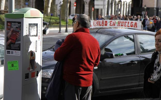 Un usuario se dispone a pagar la OTA con una manifestación de los trabajadores de fondo./Manu Cecilio