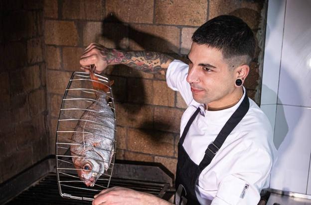 El cocinero se prepara para llevar al fuego en su rincón de Garena un besugo.